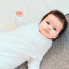 Baby in a cotton milk coloured cable edge shwrap blanket with sleeves and cuffs folded back to fit a younger baby.